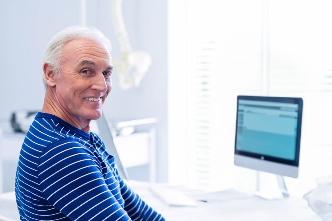 Senior Healthcare Professional Smiling at Desk with Computer and Spine Model