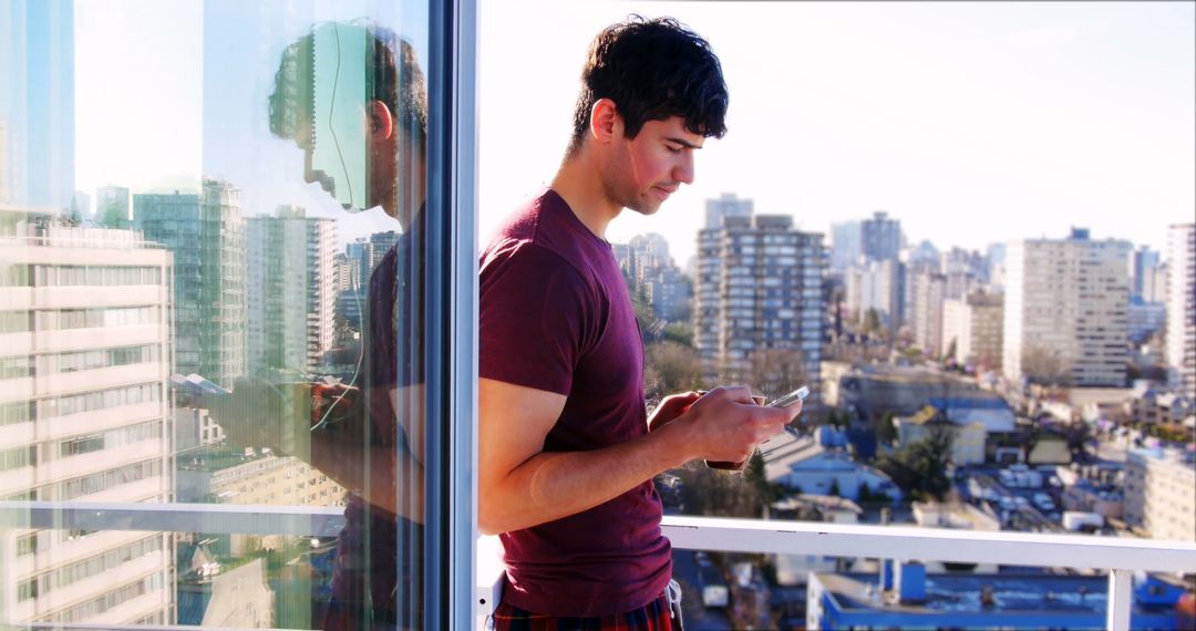 Man in Cityscape Relaxing on Balcony with Smartphone at Sunset
