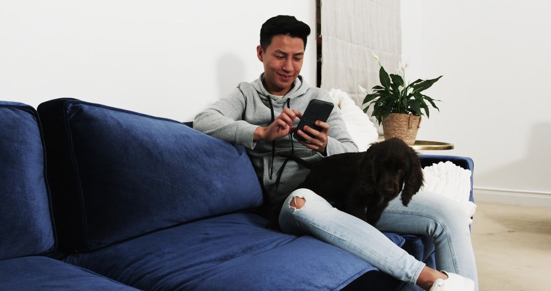 Man Relaxing with Smartphone and Puppy on Blue Sofa in Modern Living Room