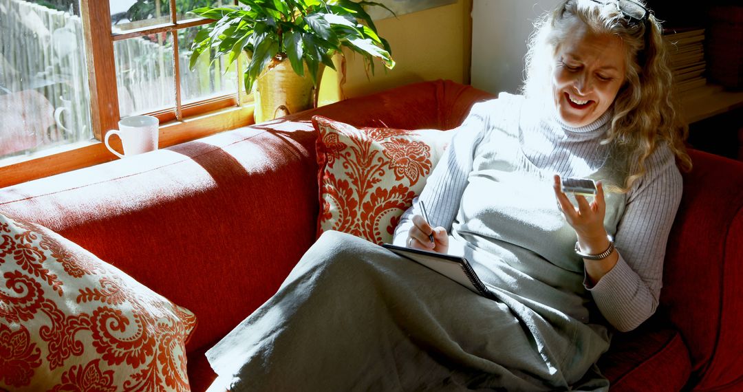 Woman Enjoying Reading and Writing Notes on Sofa by Sunlit Window - Free Images, Stock Photos and Pictures on Pikwizard.com