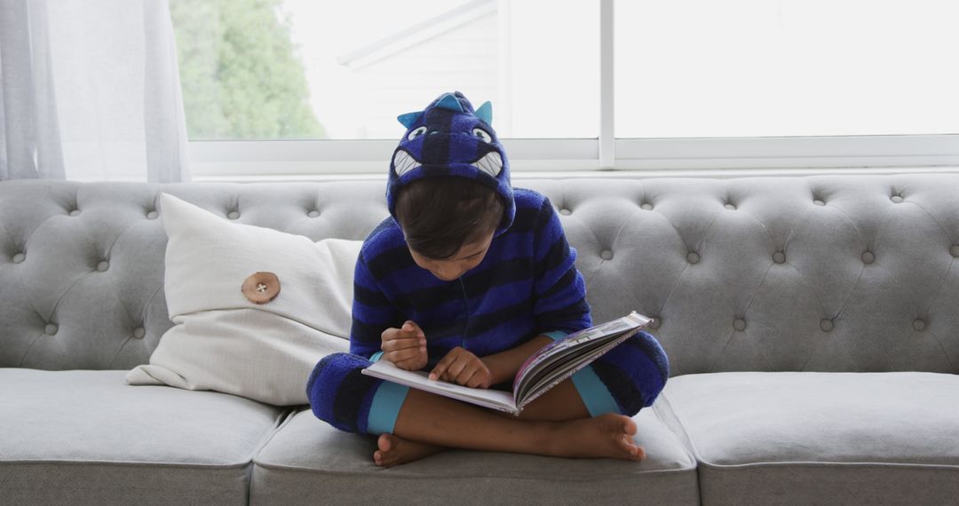 Child Reading Book on Couch Wearing Blue Dinosaur Costume - Free Images, Stock Photos and Pictures on Pikwizard.com