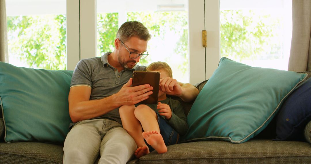 Father and Son Relaxing on Couch Reading Digital Tablet - Free Images, Stock Photos and Pictures on Pikwizard.com