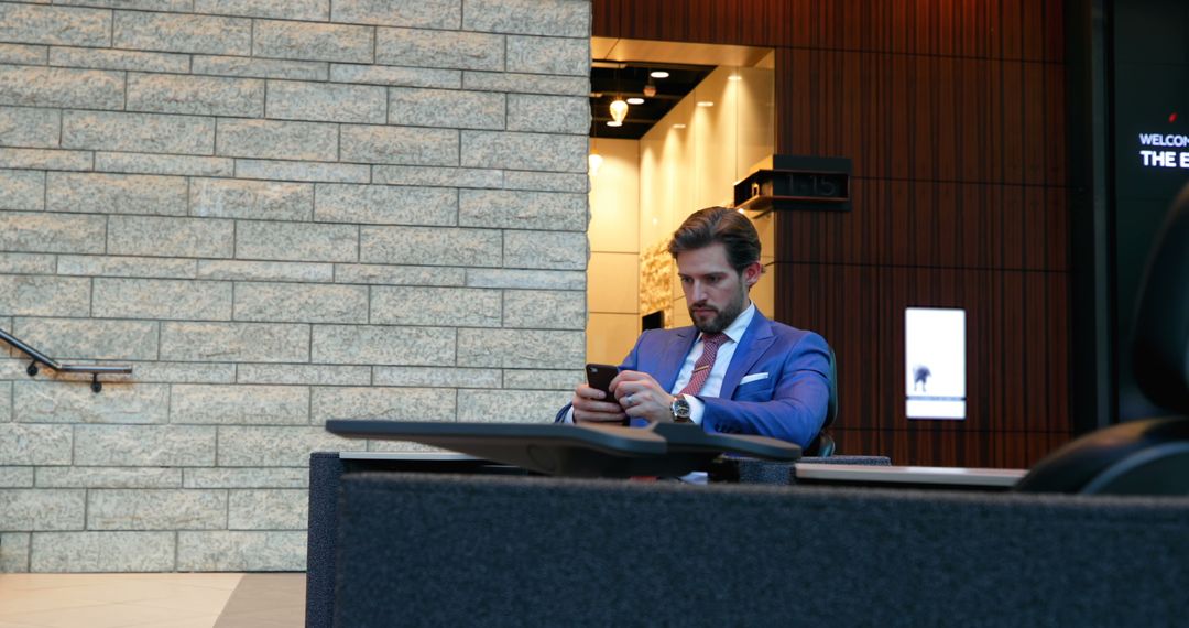 Businessman Sitting at Desk Using Smartphone Inside Modern Office Building - Free Images, Stock Photos and Pictures on Pikwizard.com