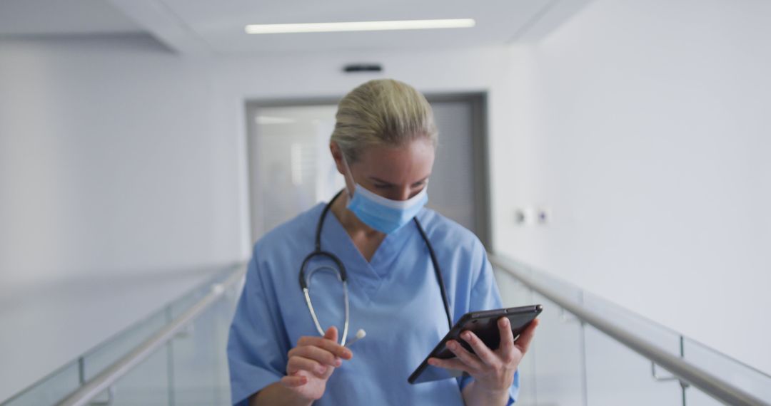 Healthcare Professional Reviewing Patient Data on Digital Tablet in Hospital Hallway - Free Images, Stock Photos and Pictures on Pikwizard.com