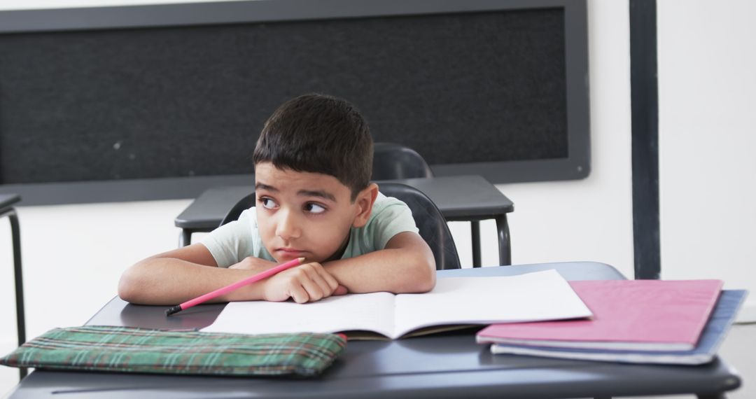 Bored Young Student in Classroom with Notebook at Desk