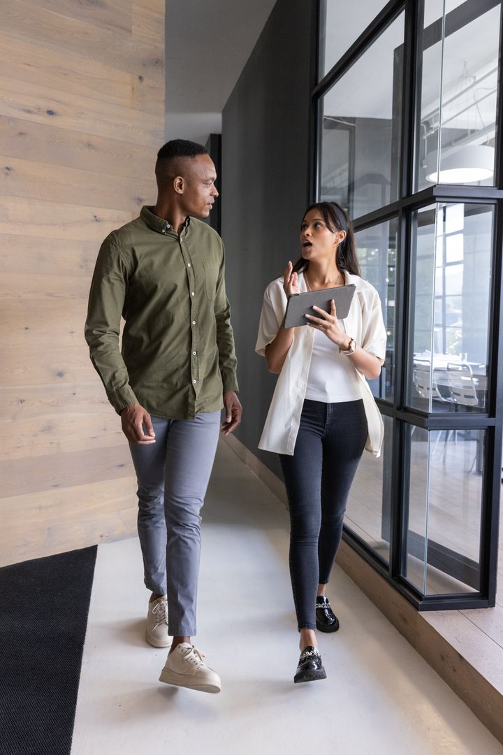 Two Professionals Discuss Work While Walking in Modern Office Hallway