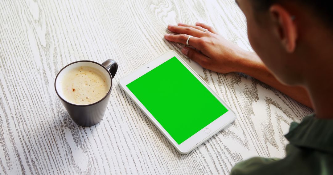 Person Holding Tablet with Green Screen Next to Coffee Cup on Wooden Table - Free Images, Stock Photos and Pictures on Pikwizard.com