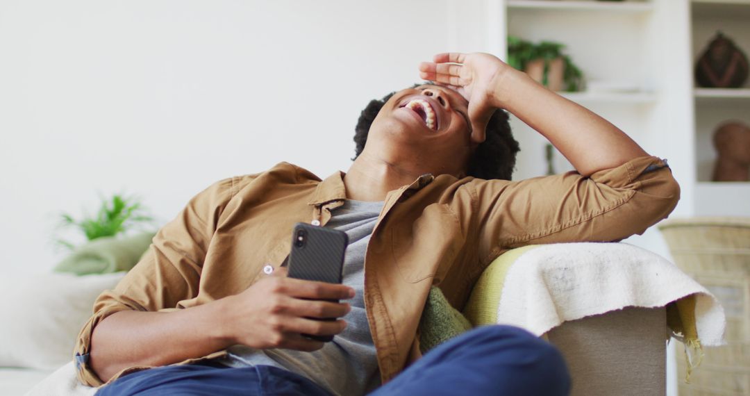 Joyful African American Man Laughing with Smartphone at Home