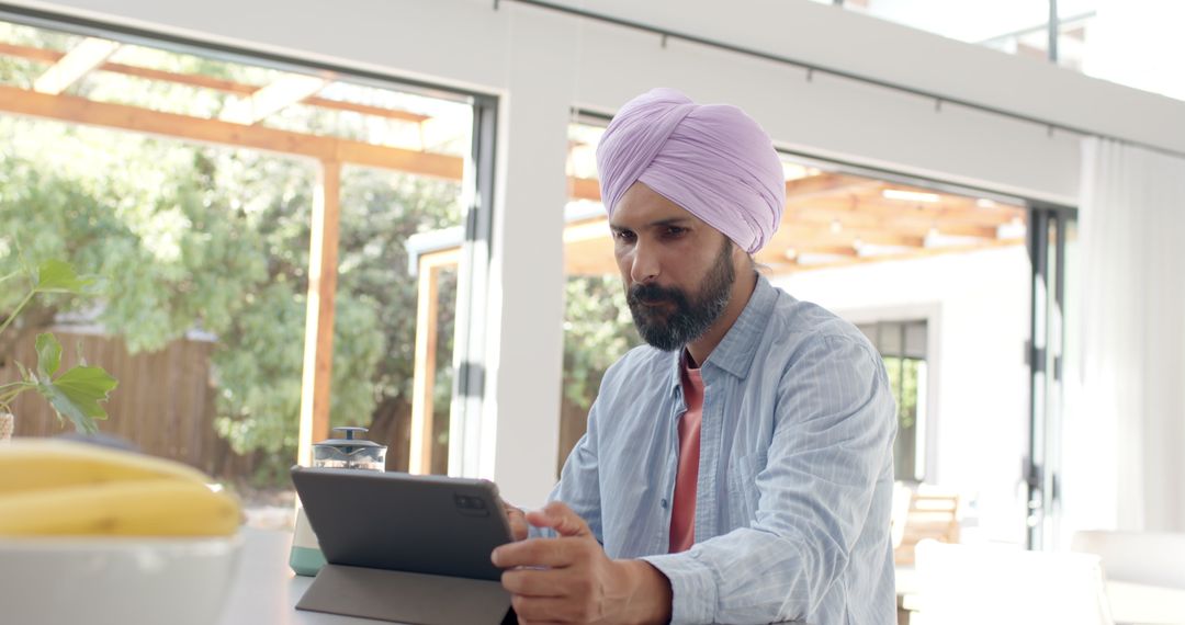 Man in Turban Using Tablet for Remote Work in Bright Modern Kitchen