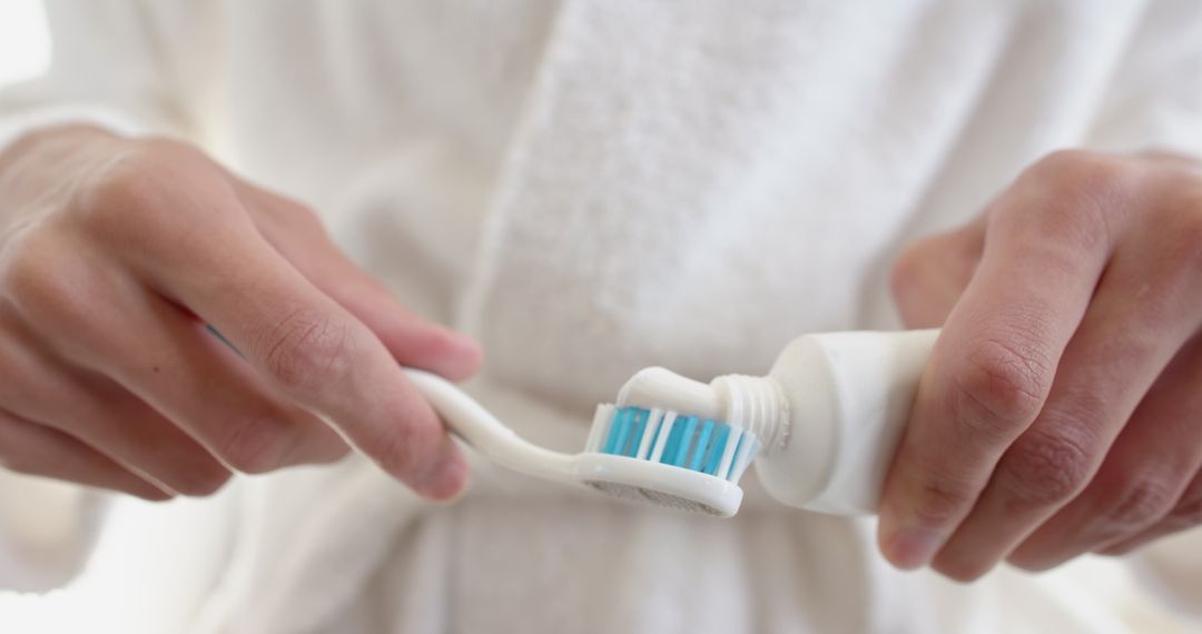 Person Applying Toothpaste onto Toothbrush in Bathroom