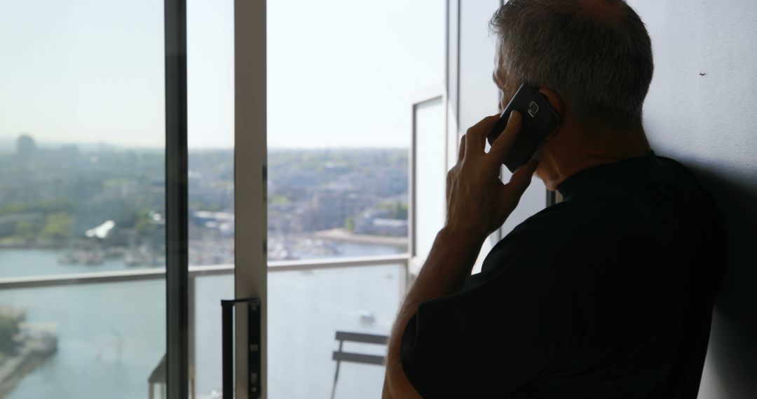 Man Talking on Phone While Looking Out Window at Cityscape - Free Images, Stock Photos and Pictures on Pikwizard.com