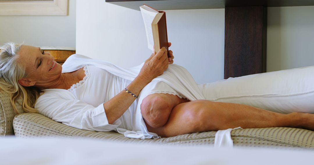 Smiling Senior Woman Reading Book on Comfortable Pillow - Free Images, Stock Photos and Pictures on Pikwizard.com