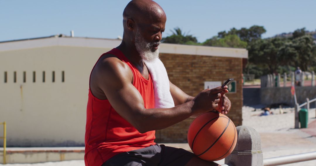 Senior Man With Basketball and Smartphone by Beach