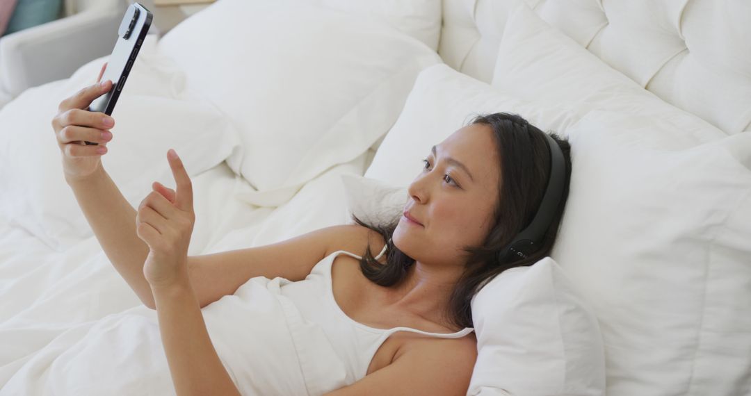 Woman Relaxing in Bed with Smartphone and Headphones - Free Images, Stock Photos and Pictures on Pikwizard.com