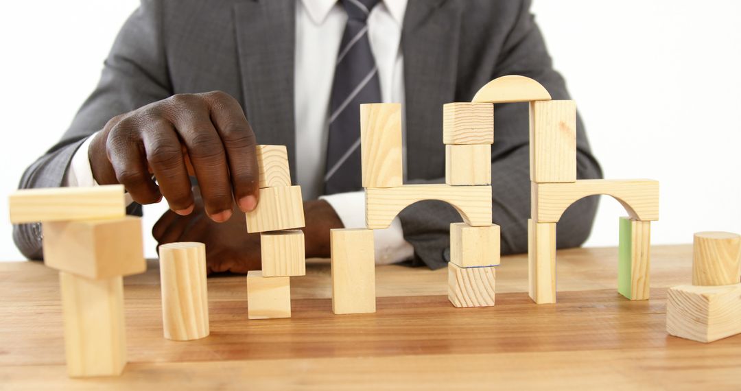 Businessman Building Structures with Wooden Blocks on Desk - Free Images, Stock Photos and Pictures on Pikwizard.com