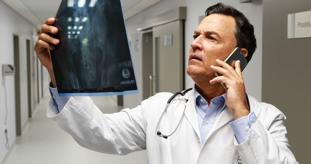 Confident Doctor Examining X-ray While Talking on Phone in Hospital Corridor - Free Images, Stock Photos and Pictures on Pikwizard.com