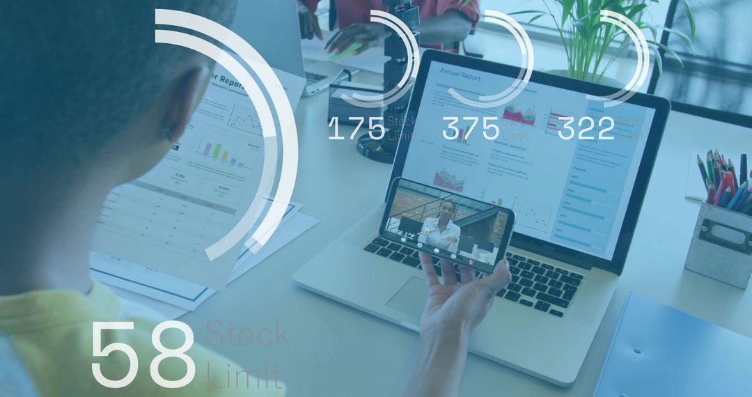 Holding phone while reviewing annual report on laptop with digital analytics overlay