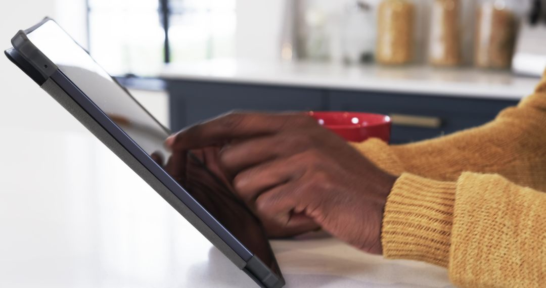 Person Using Tablet in Cozy Kitchen with Red Mug and Mustard Sweater