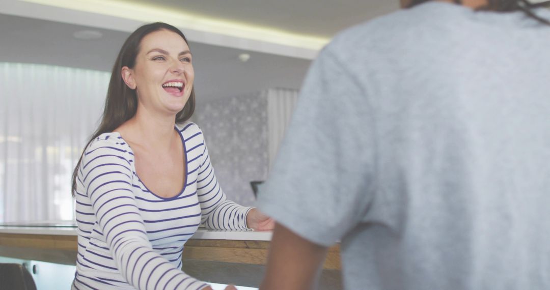 Friendly receptionist laughing and greeting guest at modern hotel front desk with wooden counter