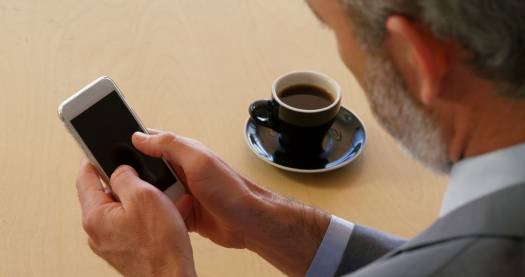 Businessman Checking Smartphone with Coffee on Desk - Free Images, Stock Photos and Pictures on Pikwizard.com