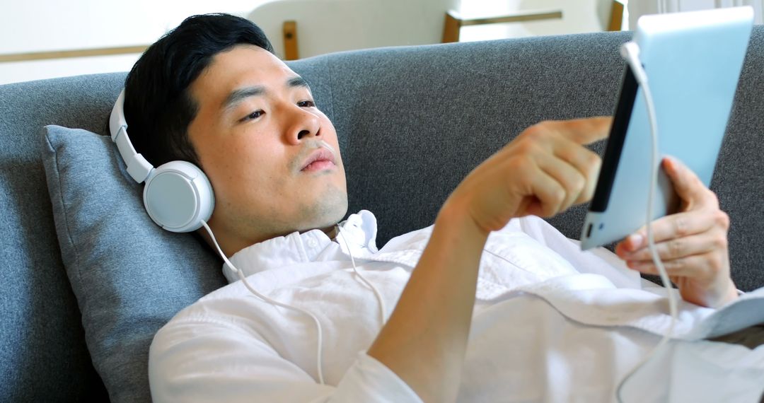 Young Male Relaxing with Headphones on Sofa Using Tablet - Free Images, Stock Photos and Pictures on Pikwizard.com