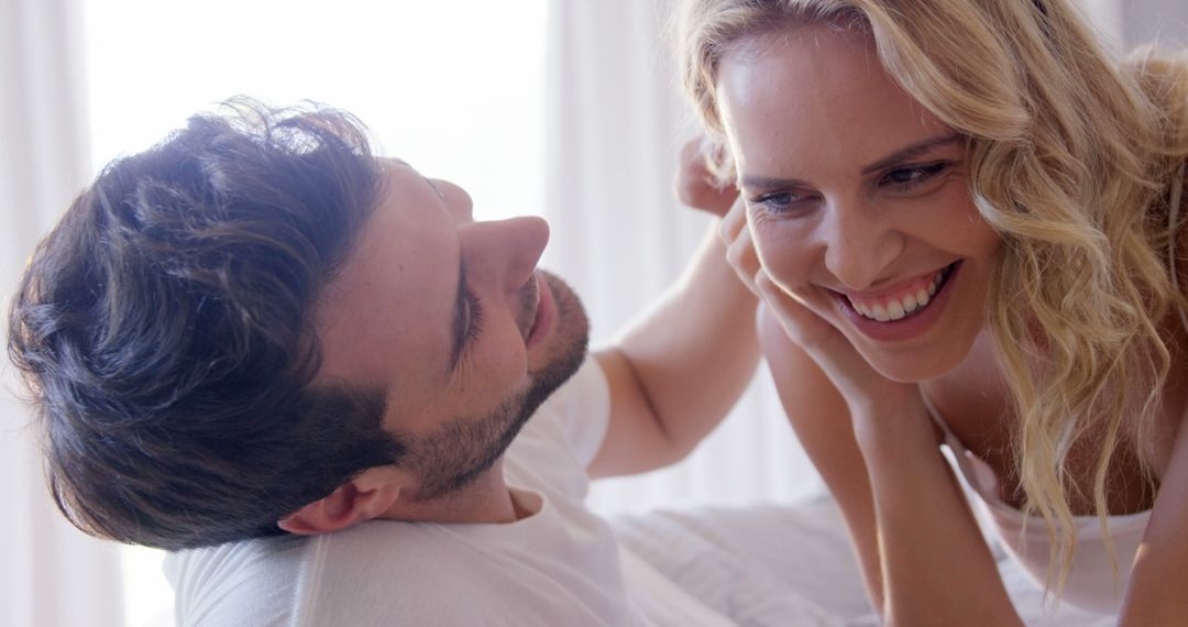 Young Couple Laughing and Embracing in Sunlit Bedroom