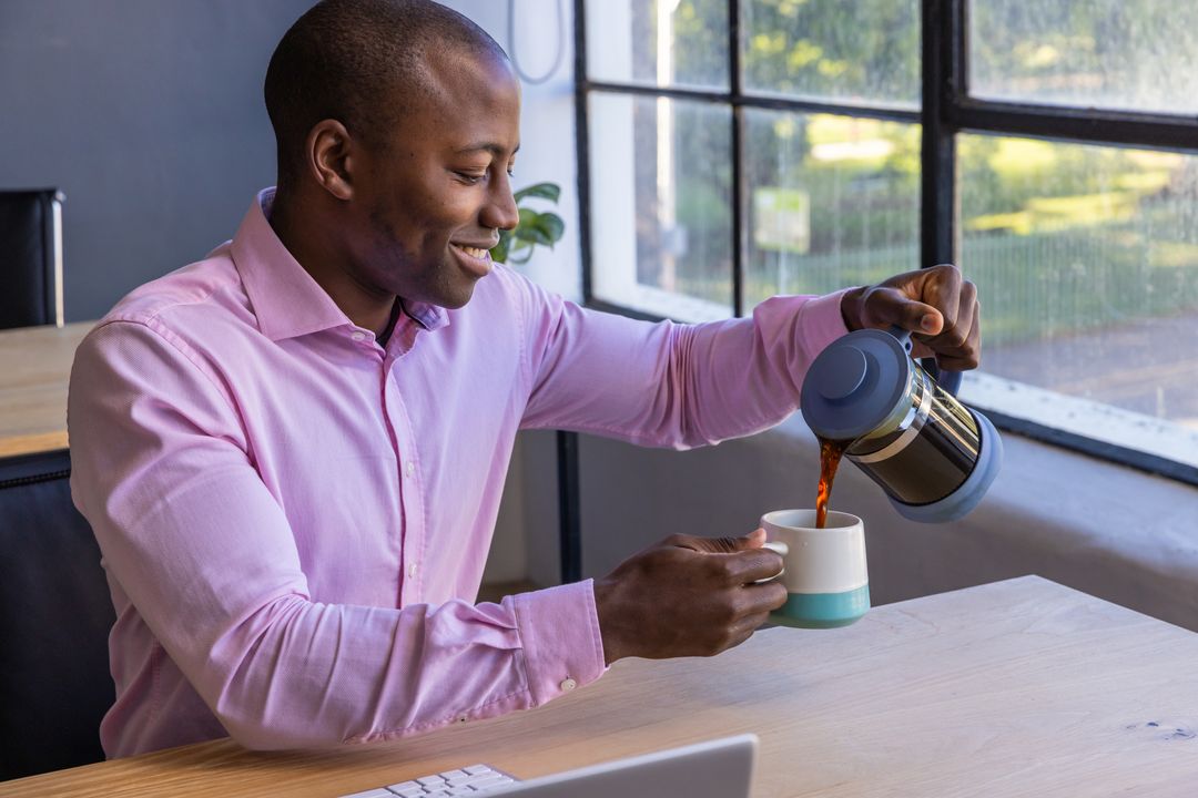Smiling Man Pouring Fresh Coffee from French Press at Desk
