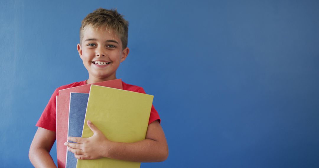 Smiling Boy Holding Colorful Notebooks Against Blue Background - Free Images, Stock Photos and Pictures on Pikwizard.com