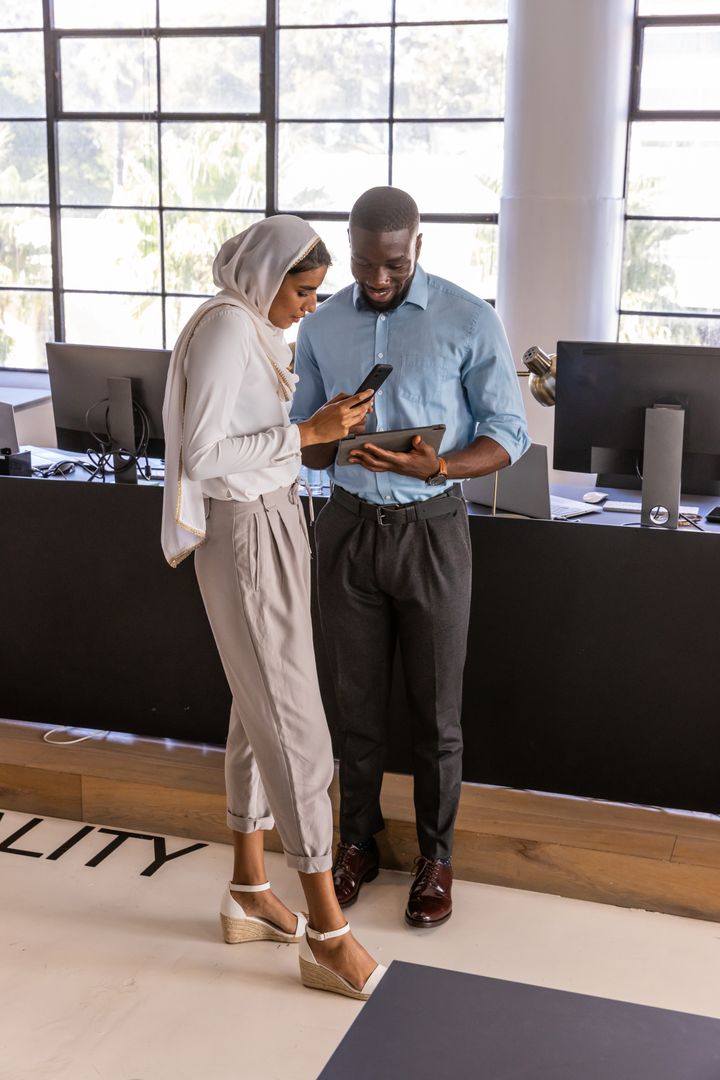 Diverse Coworkers Discuss Project with Technology in Modern Office