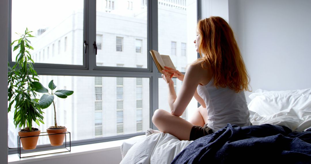 Woman Reading Book by Window with Potted Plants in Urban Apartment - Free Images, Stock Photos and Pictures on Pikwizard.com