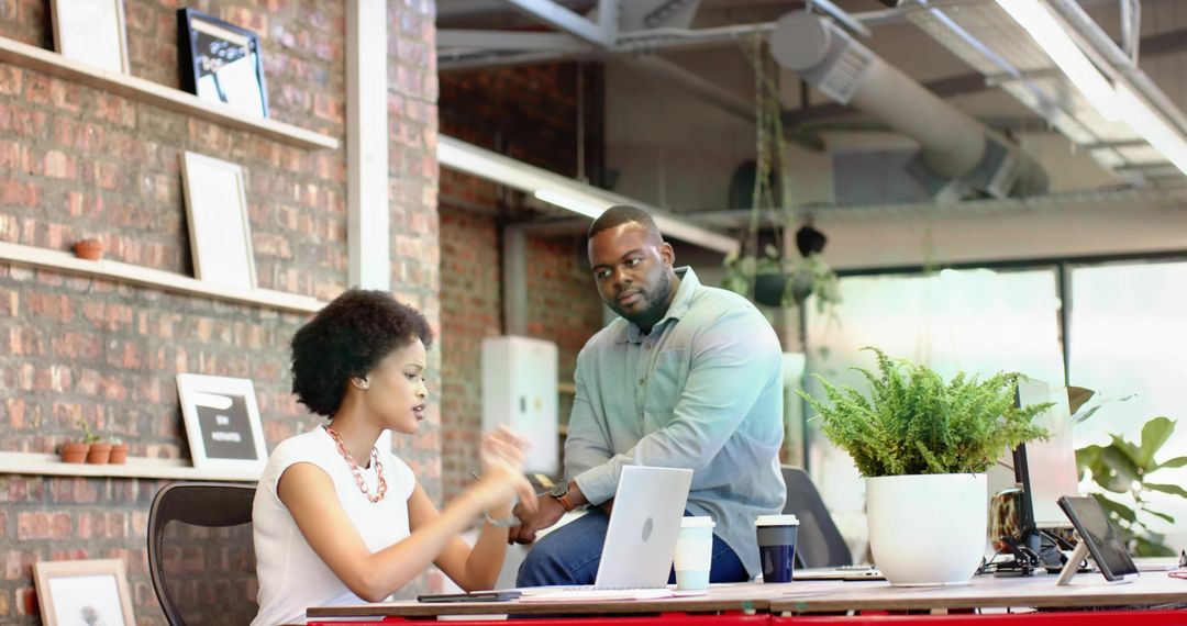 Collaborating coworkers discussing project at industrial office desk with laptop and plants