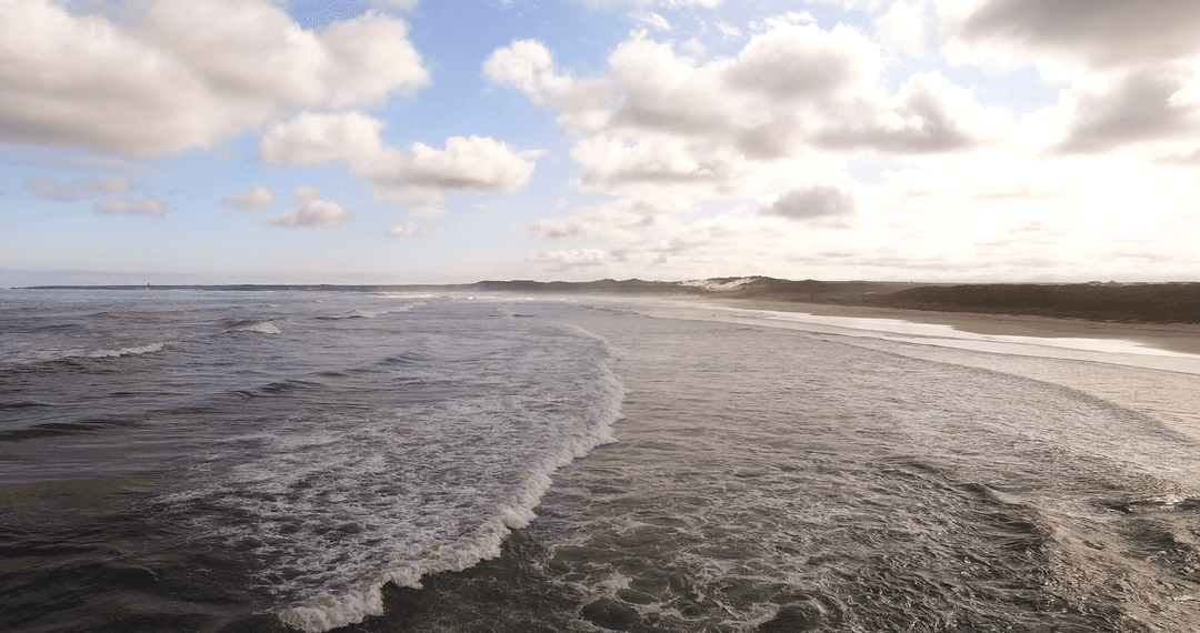 Scenic Clouds Over Transparent Ocean Waves and Sandy Beach