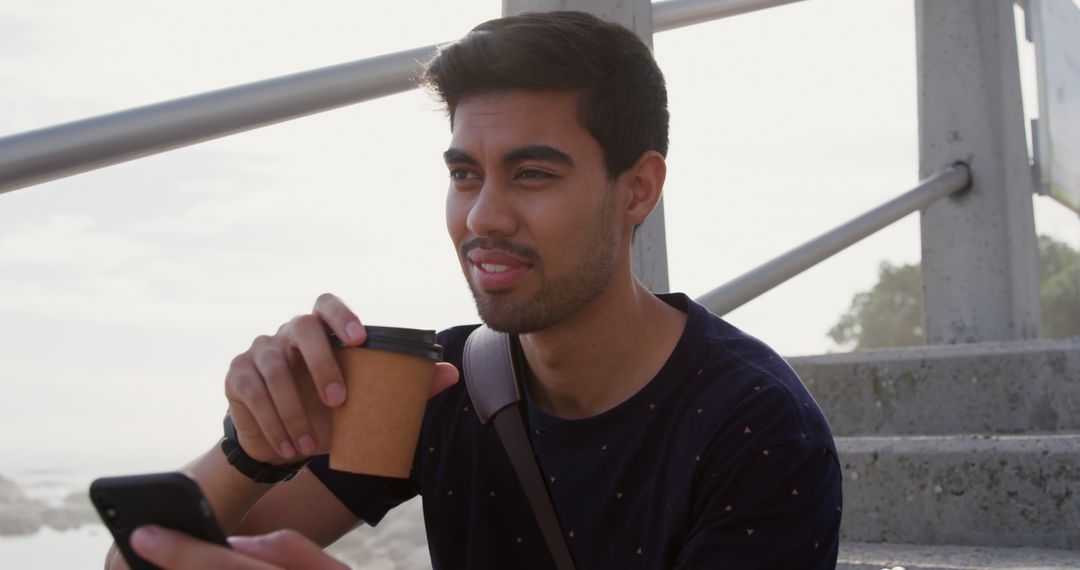 Smiling Young Man Drinking Coffee and Using Smartphone Outdoors - Free Images, Stock Photos and Pictures on Pikwizard.com