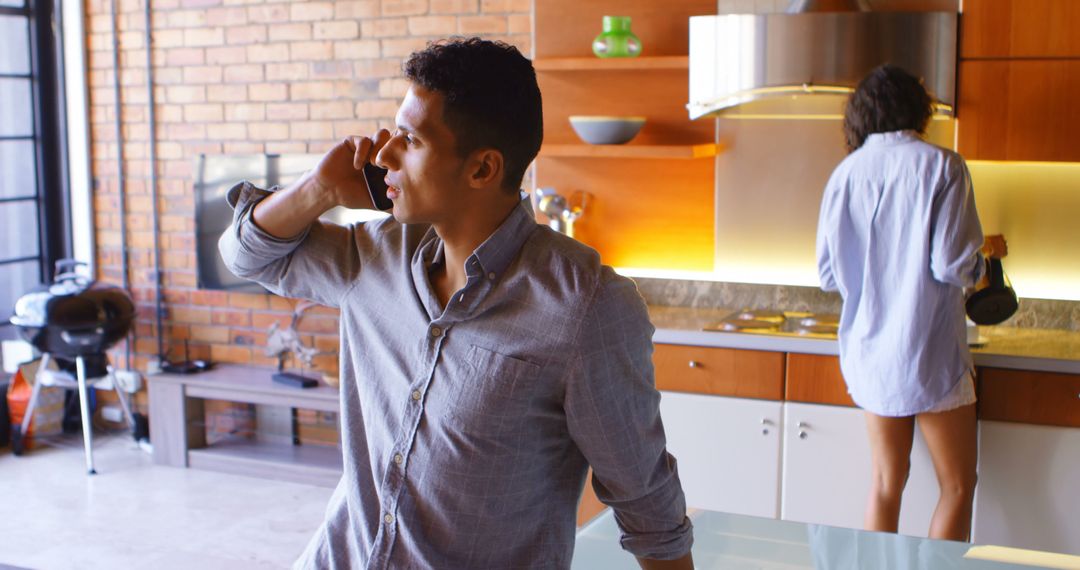 Man talking on phone while woman cooking breakfast in modern kitchen - Free Images, Stock Photos and Pictures on Pikwizard.com