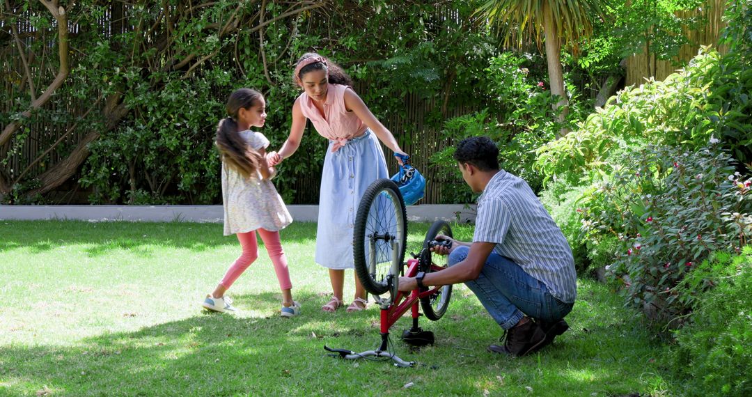 Father Repairing Bicycle with Daughters in Sunny Backyard