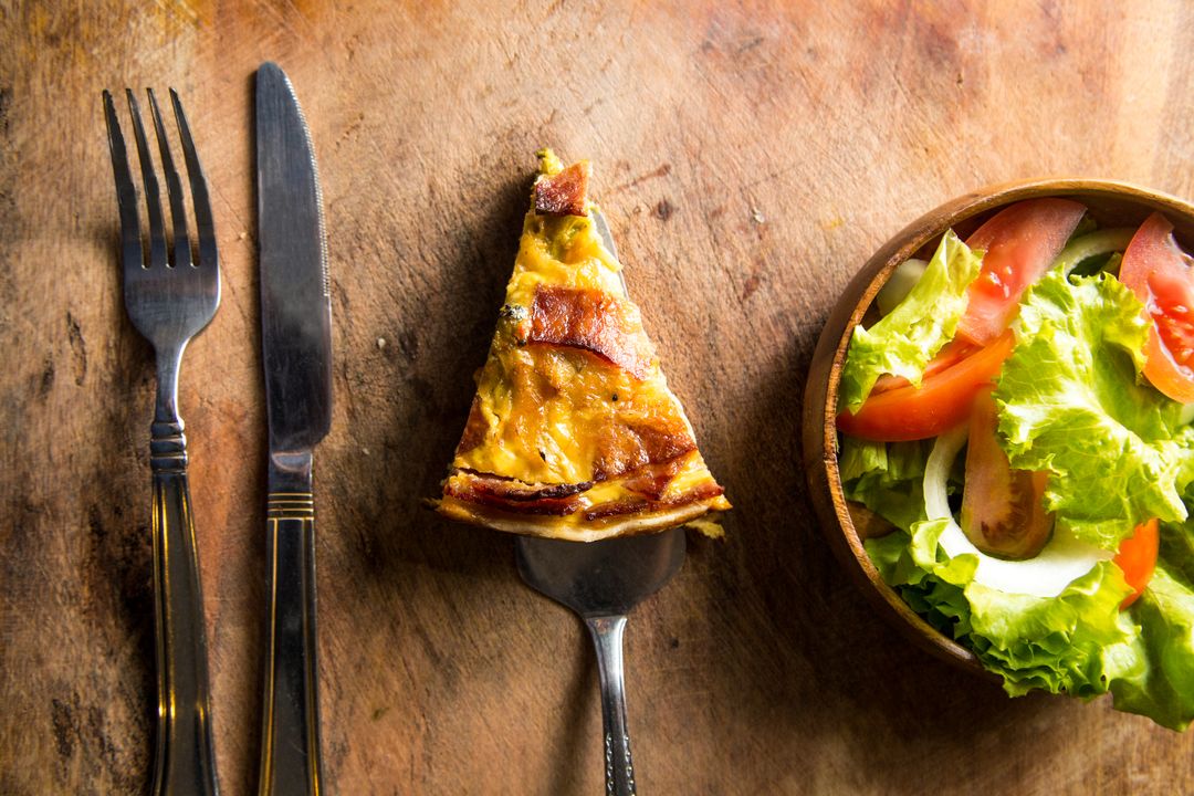 Serving rustic bacon quiche slice paired with fresh garden salad on wooden board