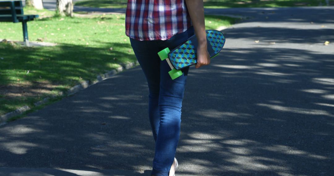 Person walking through park holding skateboard - Free Images, Stock Photos and Pictures on Pikwizard.com