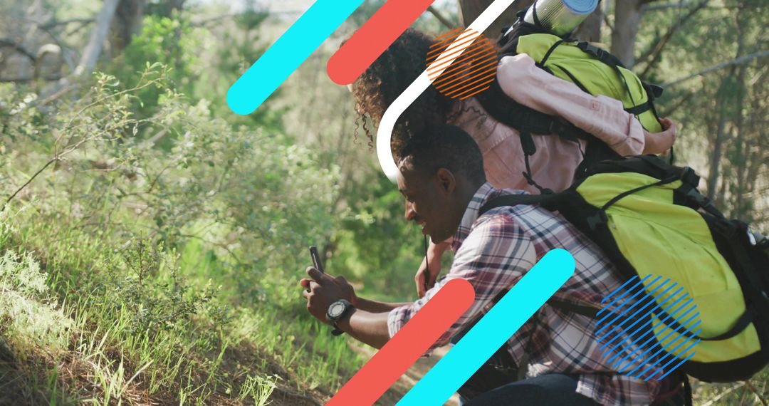 Couple hiking in sunlit woodland checking smartphone for navigation with lime green backpacks