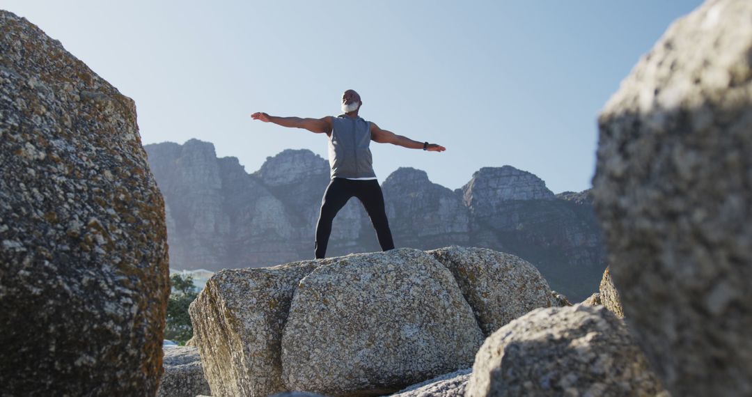 Man Standing on Rocks with Arms Outstretched in Mountain Landscape - Free Images, Stock Photos and Pictures on Pikwizard.com