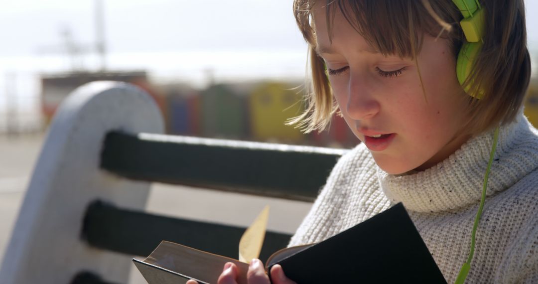 Child Reading a Book Wearing Headphones on a Bench Outdoors - Free Images, Stock Photos and Pictures on Pikwizard.com