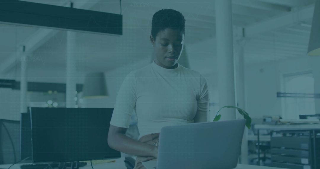 Professional woman standing and working on laptop in modern open-plan office with plant