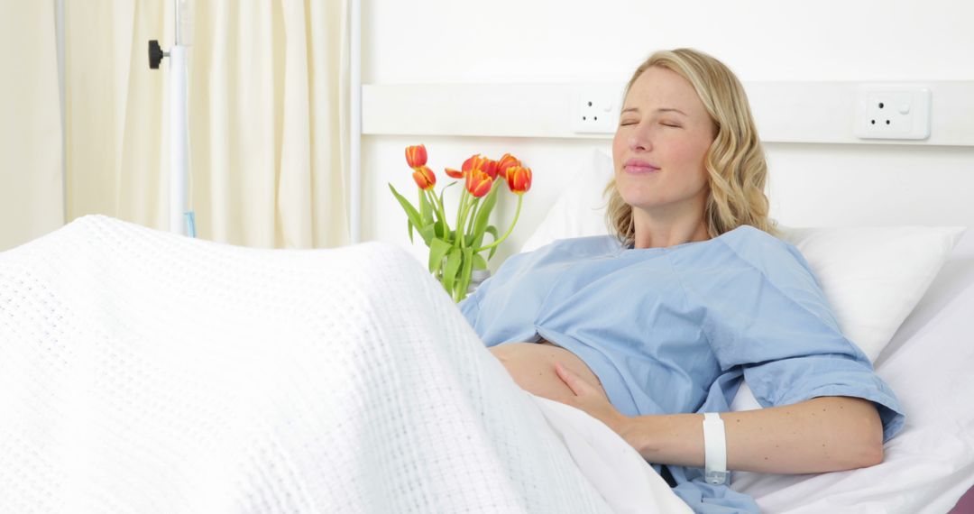 Pregnant woman resting in hospital bed smiling with tulips in background - Free Images, Stock Photos and Pictures on Pikwizard.com