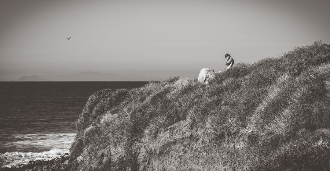 Solitary Individual Sitting on Coastal Cliff Overlooking the Ocean - Free Images, Stock Photos and Pictures on Pikwizard.com