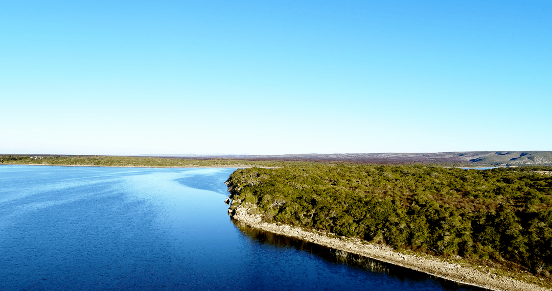 Transparent Water Embracing Grassy Hill Beneath Clear Sky Serenity