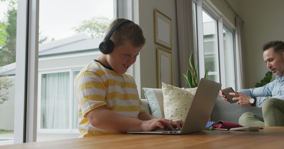 Young Boy with Down Syndrome Using Laptop with Headphones, Parent in Background - Free Images, Stock Photos and Pictures on Pikwizard.com