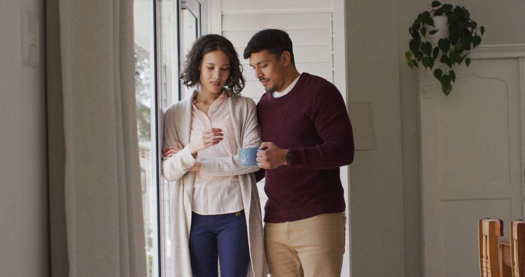 Happy hispanic couple standing in window embracing having coffee - Free Images, Stock Photos and Pictures on Pikwizard.com