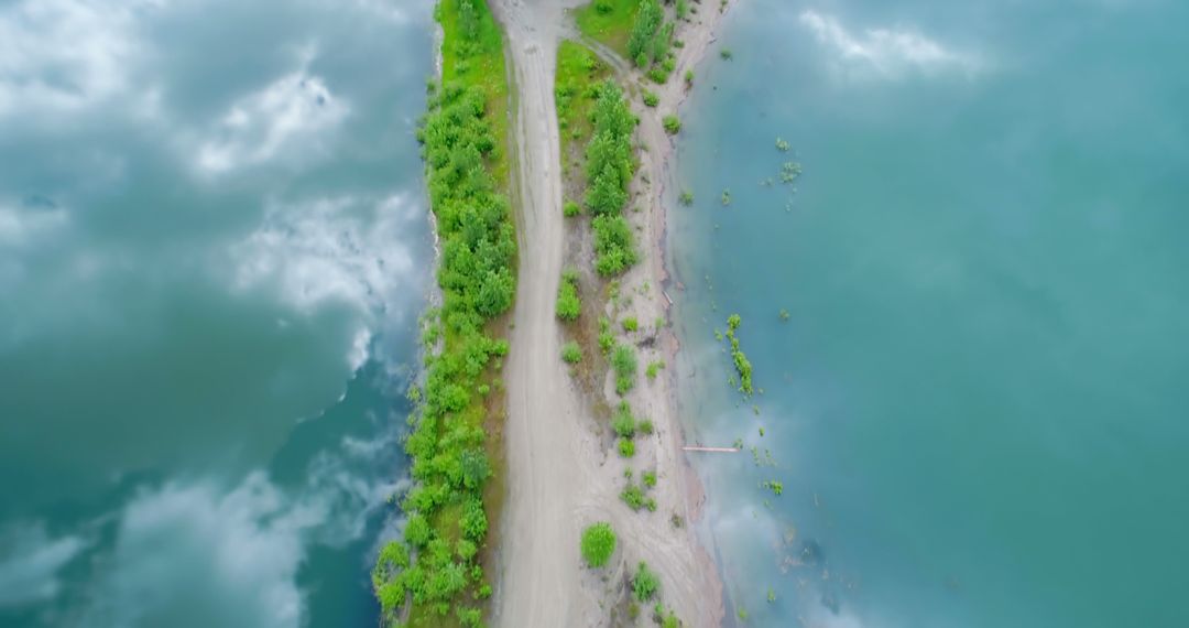 An aerial view showcases a serene dirt path between verdant terrain and calm waters. - Free Images, Stock Photos and Pictures on Pikwizard.com
