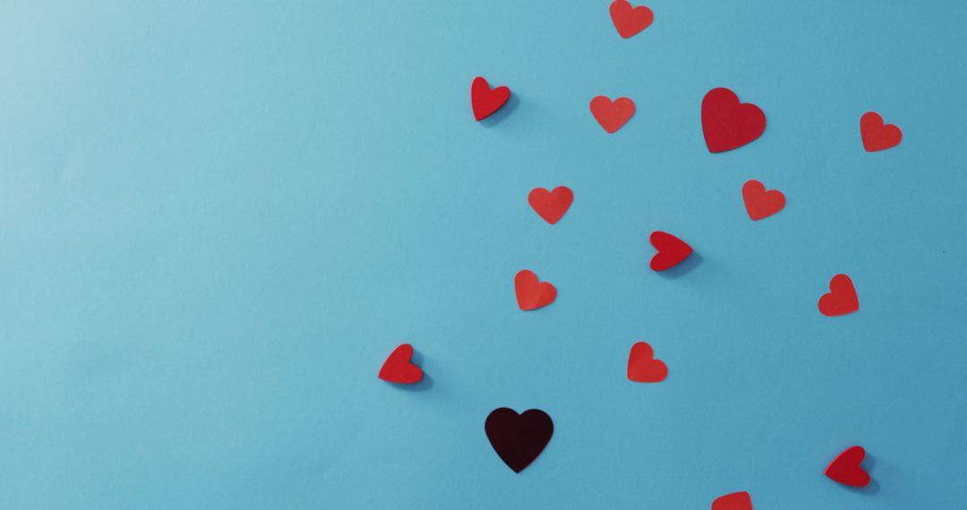 Scattered Red and Black Paper Hearts on Blue Backdrop