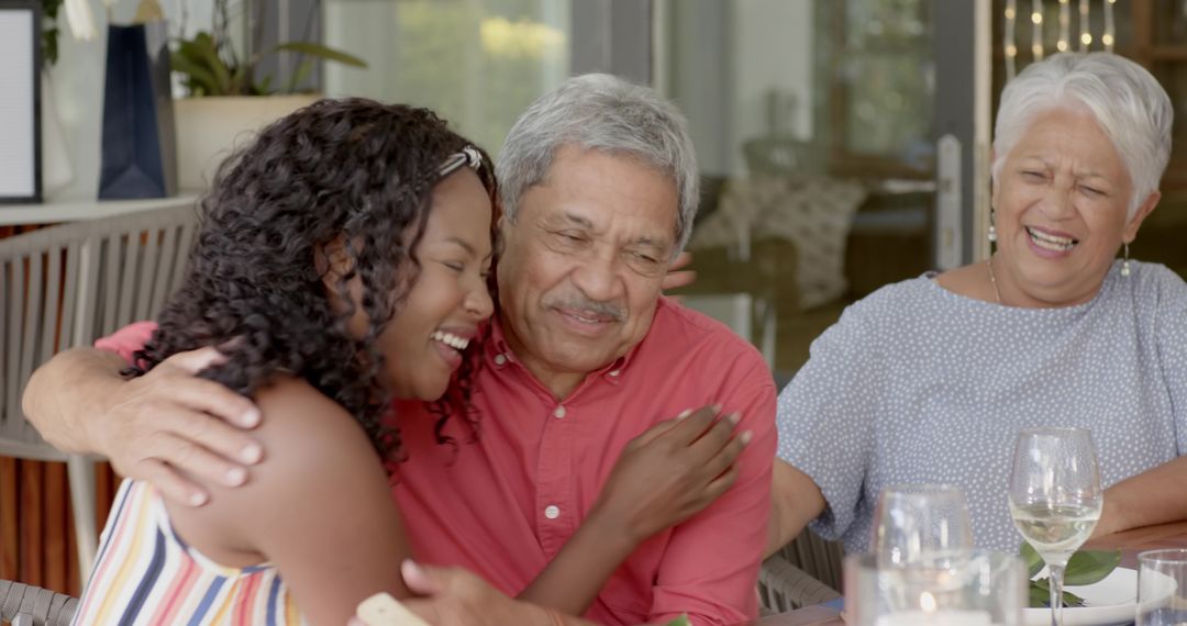 Multigenerational family hugging and laughing around sunroom table with wine glasses