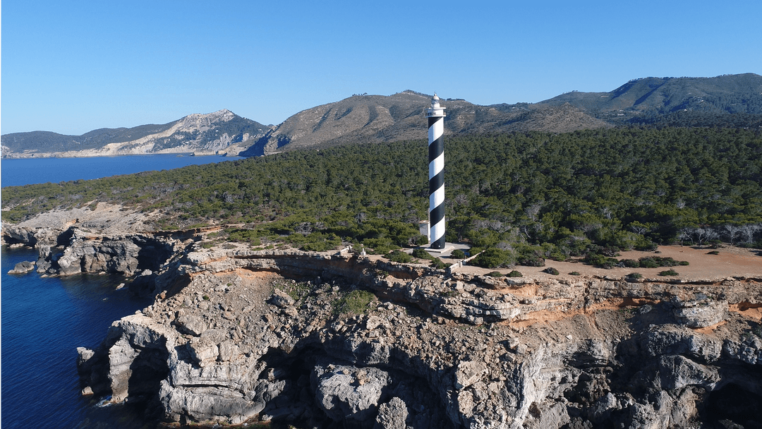 High Angle View of Striped Lighthouse on Rocky Coastline with Clear Sky